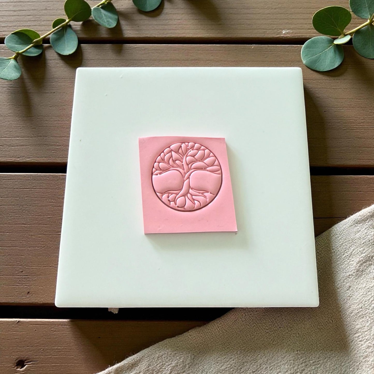 Pink clay square showing embossed tree of life symbol on white tile