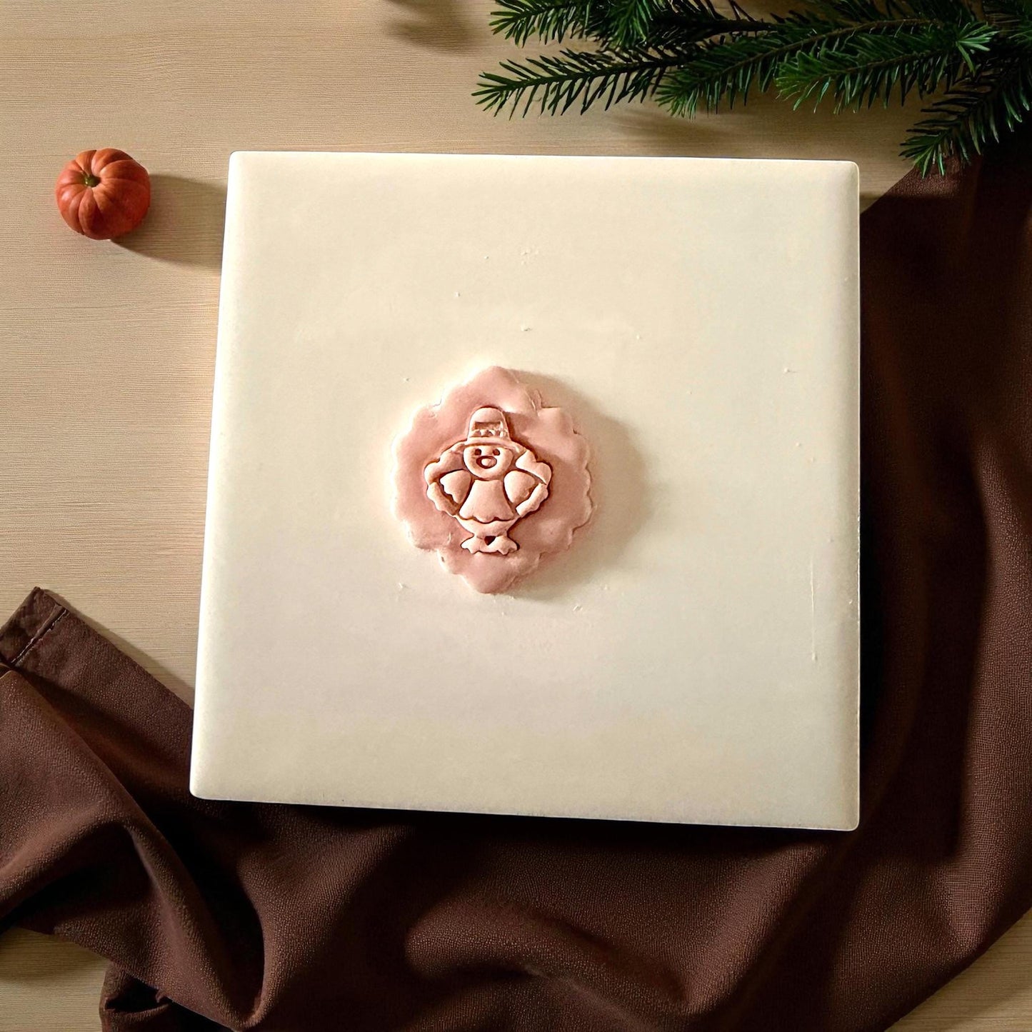 Pilgrim turkey clay imprint centered on white tile with pumpkin and greenery