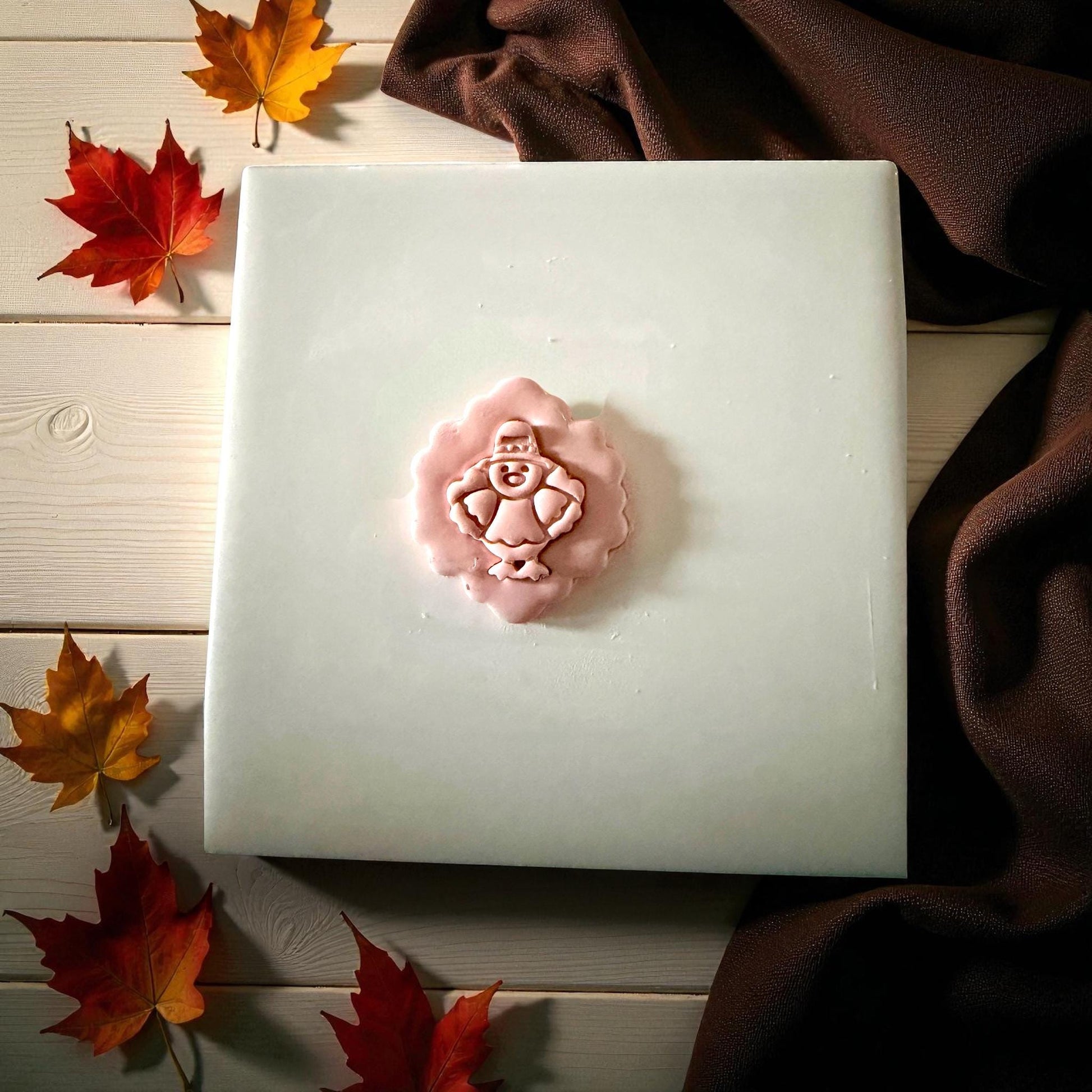 Pilgrim turkey clay imprint centered on white tile with pumpkin and greenery