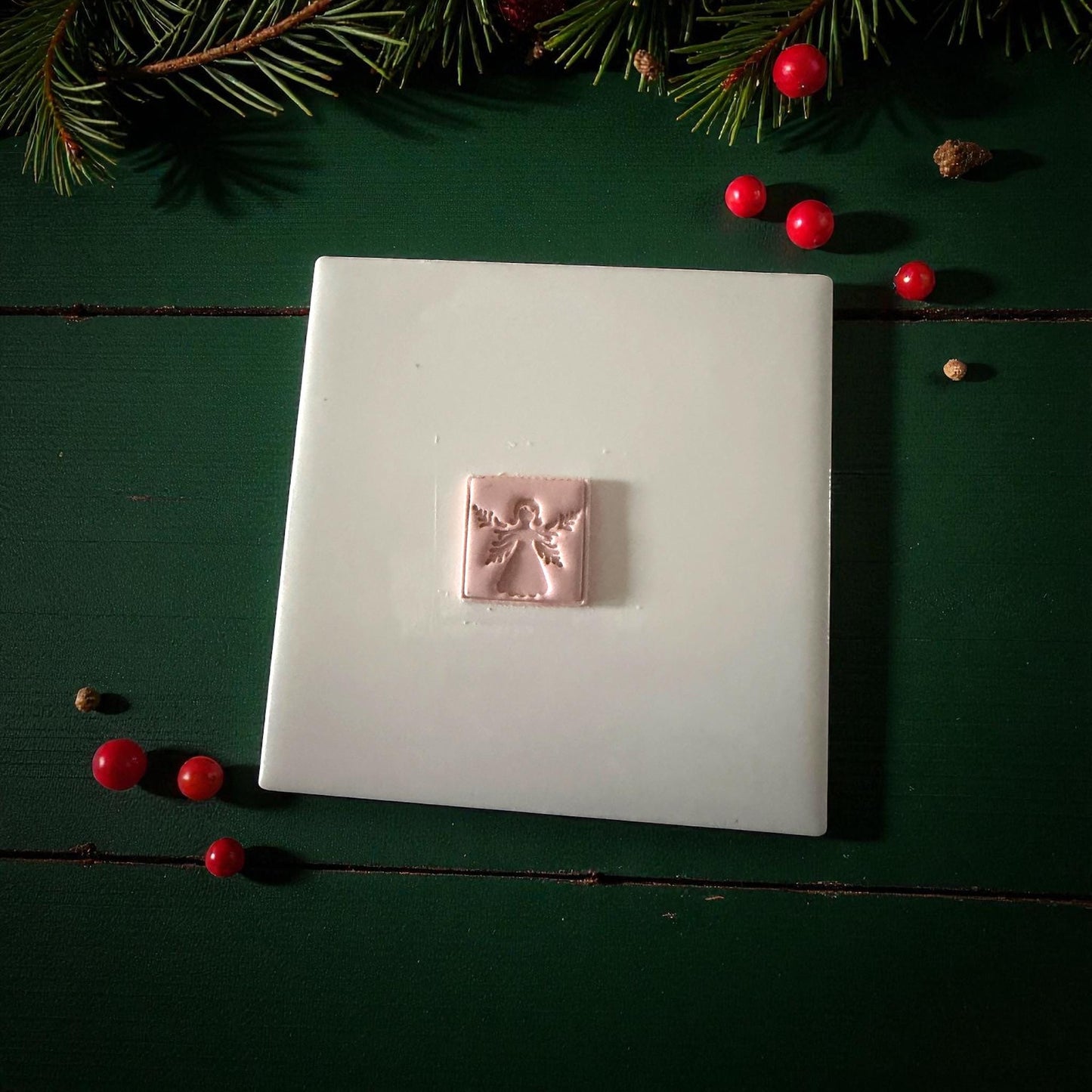 Pink clay square angel imprint centered on white tile with Christmas ornaments