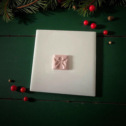 Pink clay square angel imprint centered on white tile with Christmas ornaments