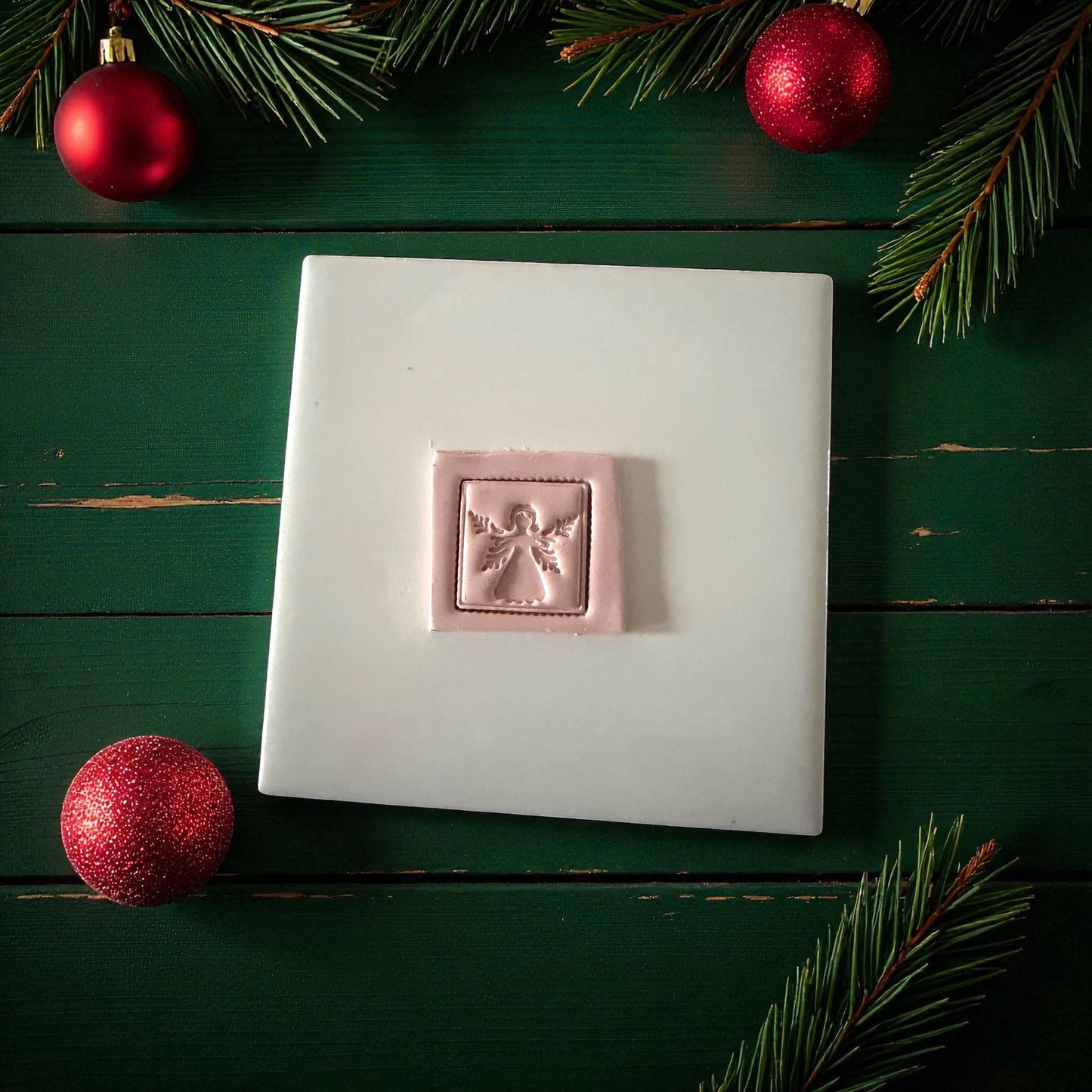 Pink clay square angel imprint centered on white tile with Christmas ornaments