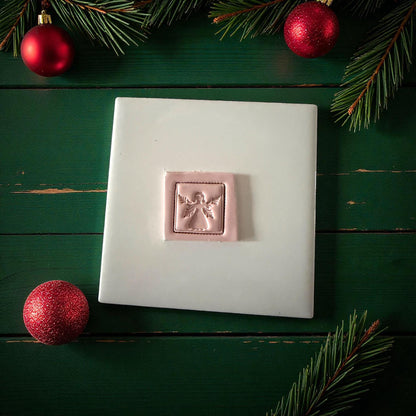 Pink clay square angel imprint centered on white tile with Christmas ornaments