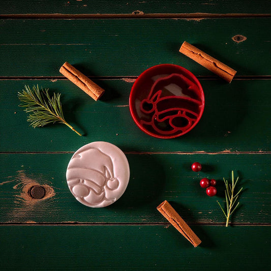 Santa clay imprint and red cutter displayed together on green background with cinnamon sticks and pine sprigs