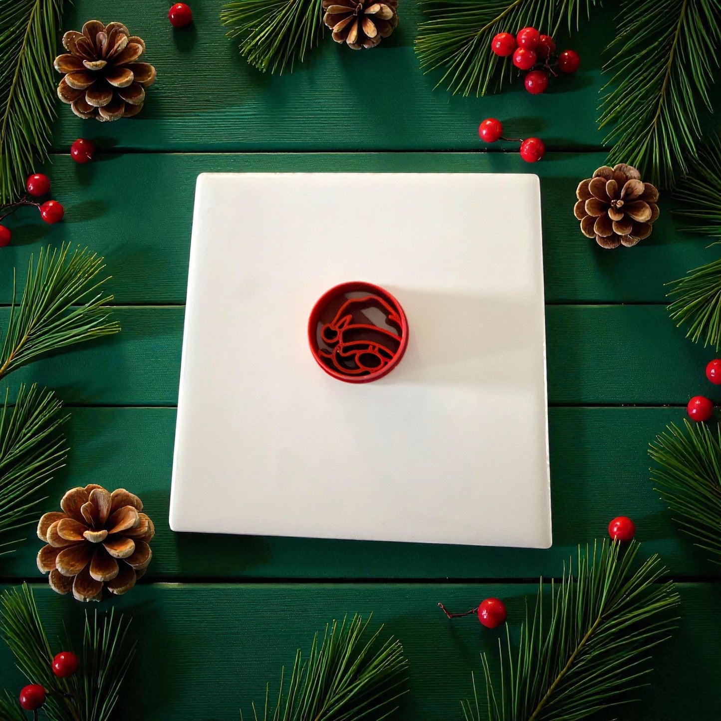 Red round Santa cutter centered on white tile with pinecones and berries