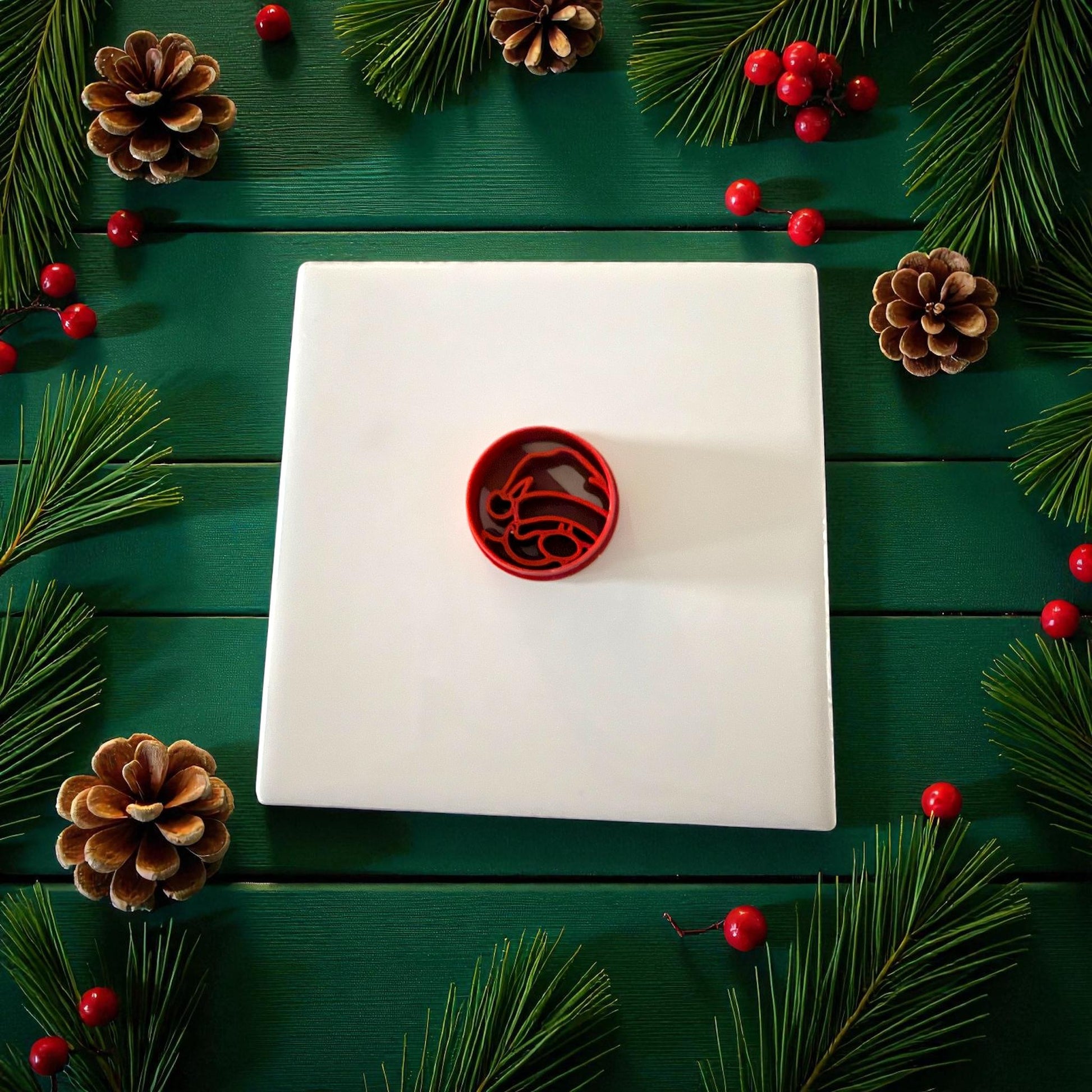 Red round Santa cutter centered on white tile with pinecones and berries