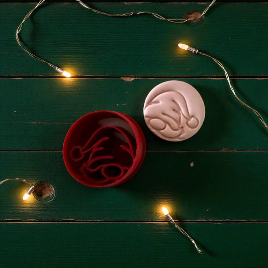 Red round gnome cutter beside pink imprint with snowflake and holly branch decor