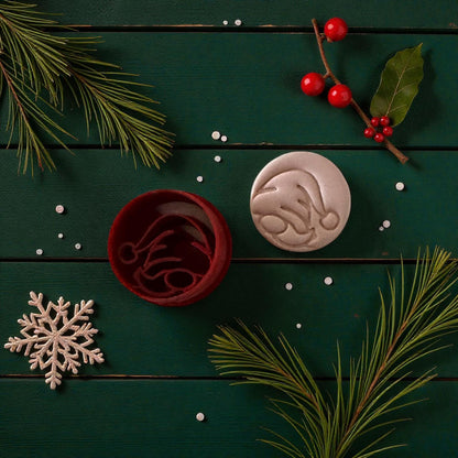 Red round gnome cutter beside pink imprint with snowflake and holly branch decor