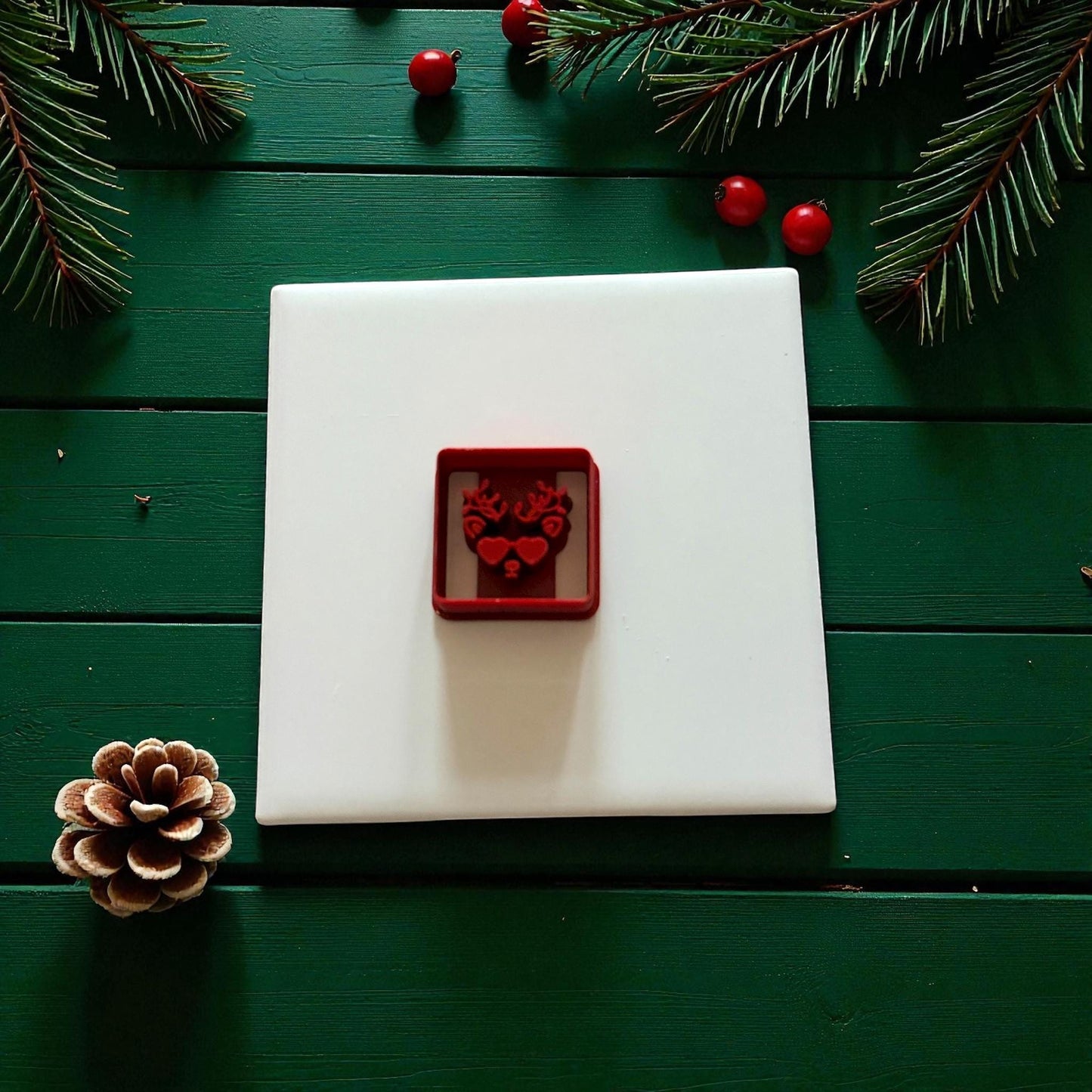 Red reindeer cutter centered on white tile with pine branches and berries