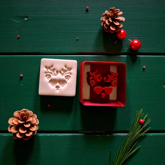 Red reindeer cutter beside clay imprint with pinecone and holly accents