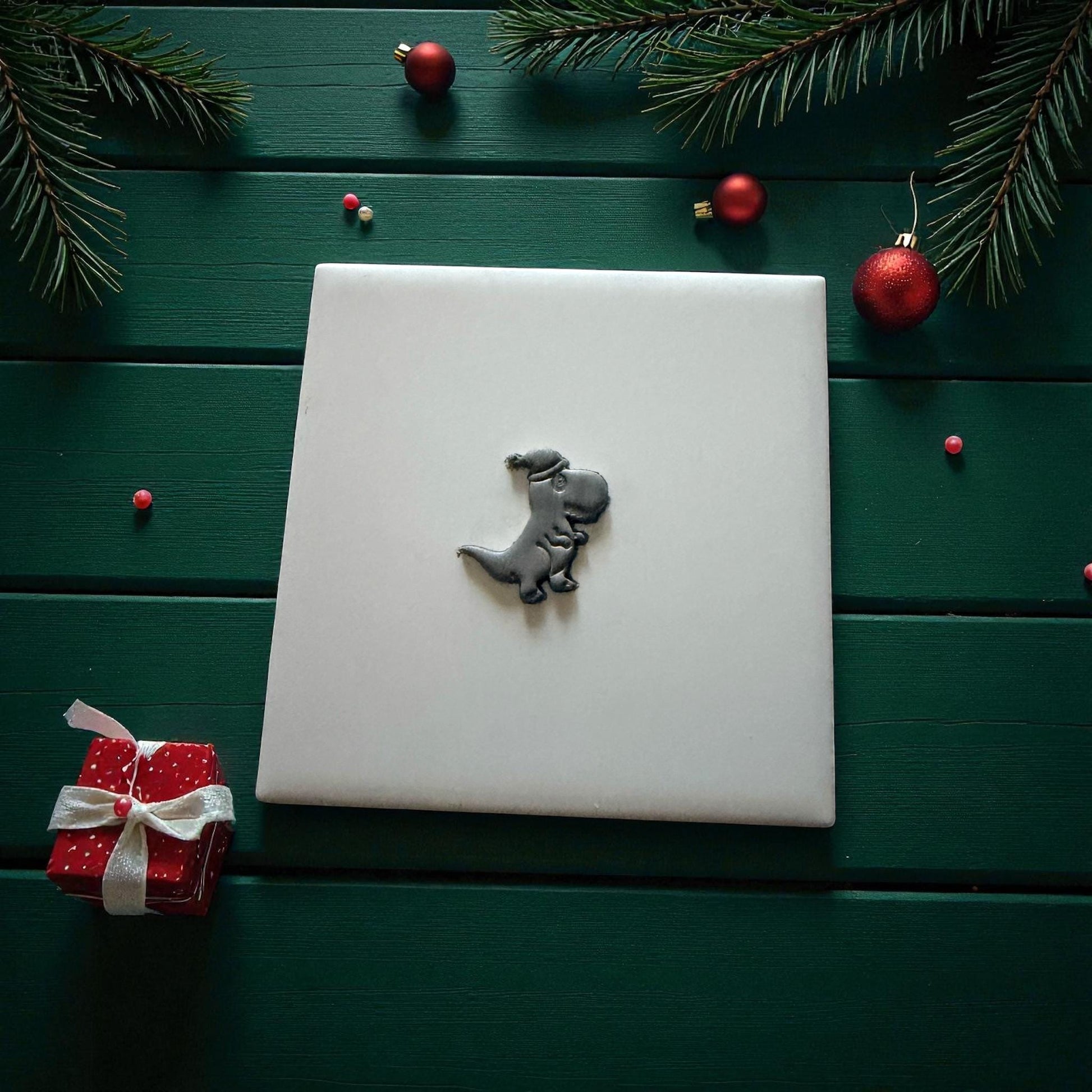Small gray dino clay imprint centered on white tile with gift box and ornaments