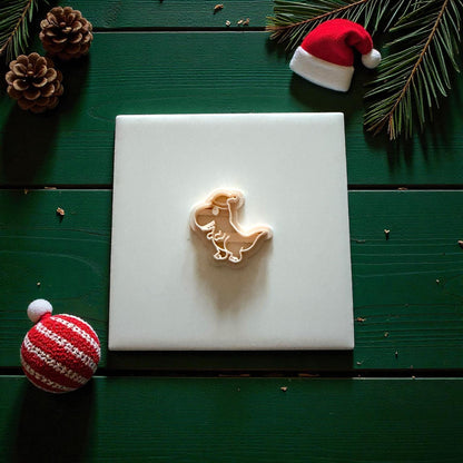 Cream dinosaur cutter on white tile with Christmas ornaments and mini Santa hat