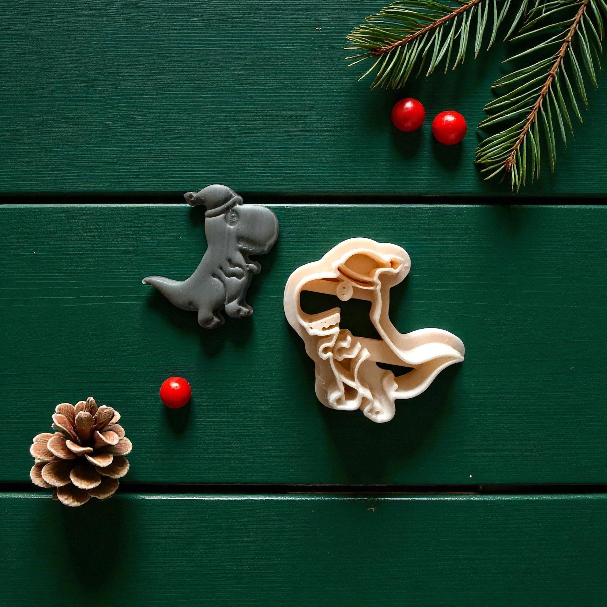 Gray and cream dinosaur cutters side by side on green background with pine and berries