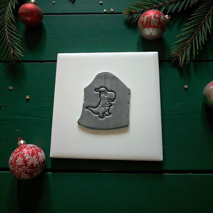 Gray dinosaur clay imprint on white tile with Christmas ornaments and pine branches