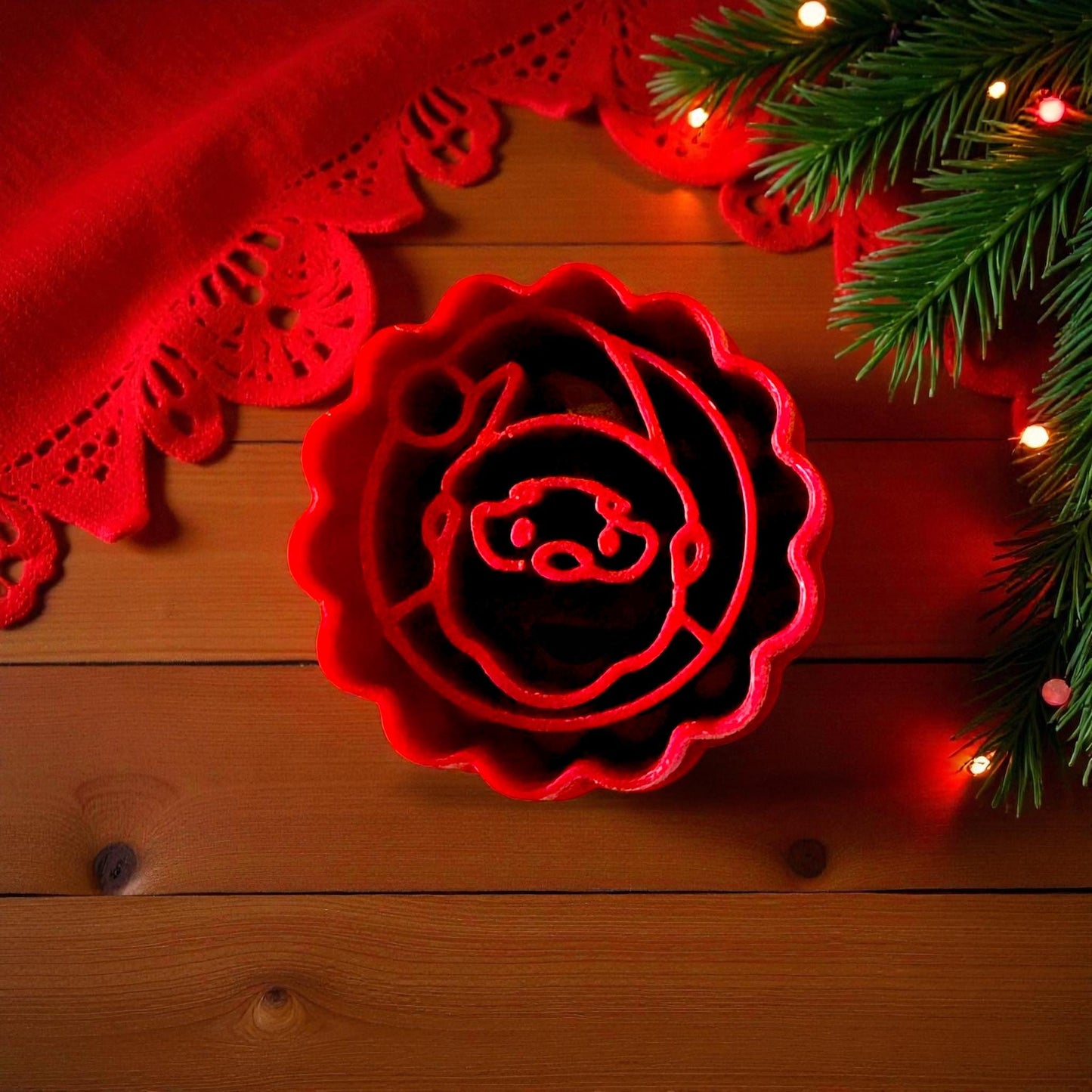 Red scalloped Santa clay cutter surrounded by pine branches and red holiday fabric