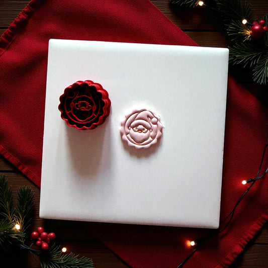 Santa clay imprint beside red scalloped cutter on white tile with festive greenery