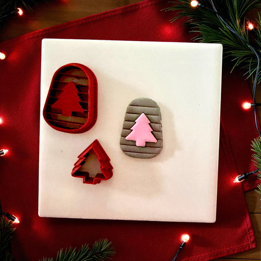 Red arch and tree cutters next to pink tree clay imprint on white tile with Christmas decor