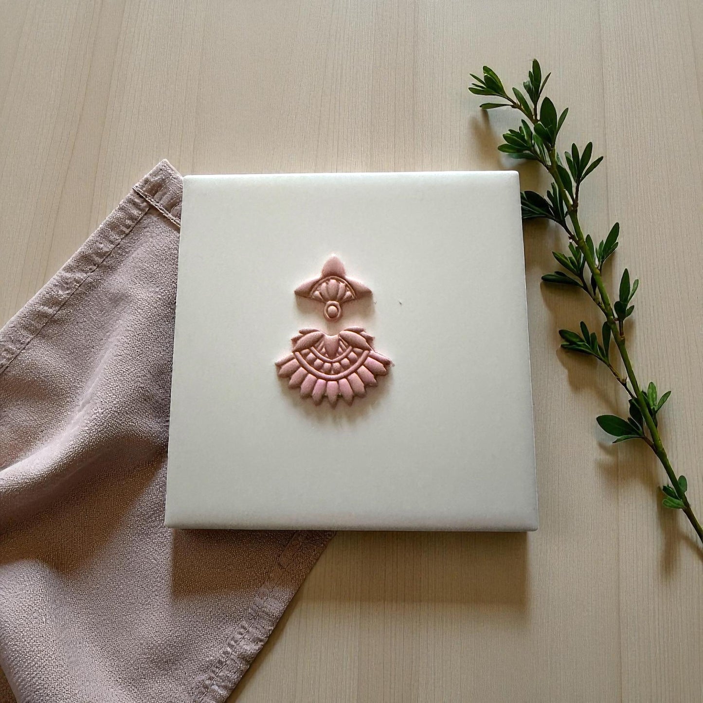 Small boho fan clay imprint centered on white tile with soft pink napkin