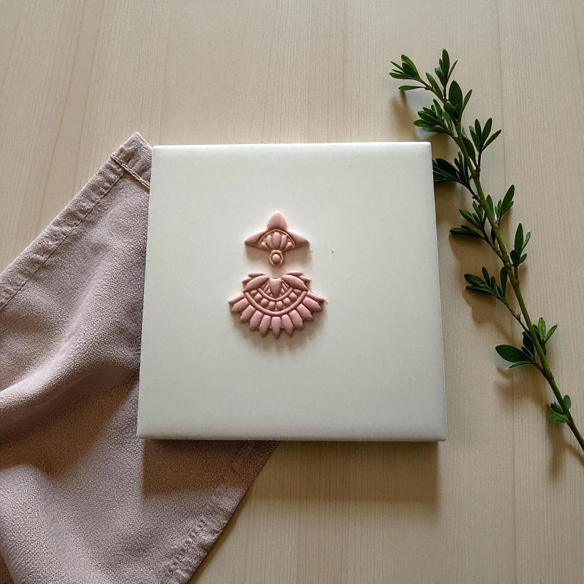 Small boho fan clay imprint centered on white tile with soft pink napkin