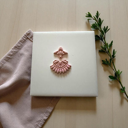 Small boho fan clay imprint centered on white tile with soft pink napkin