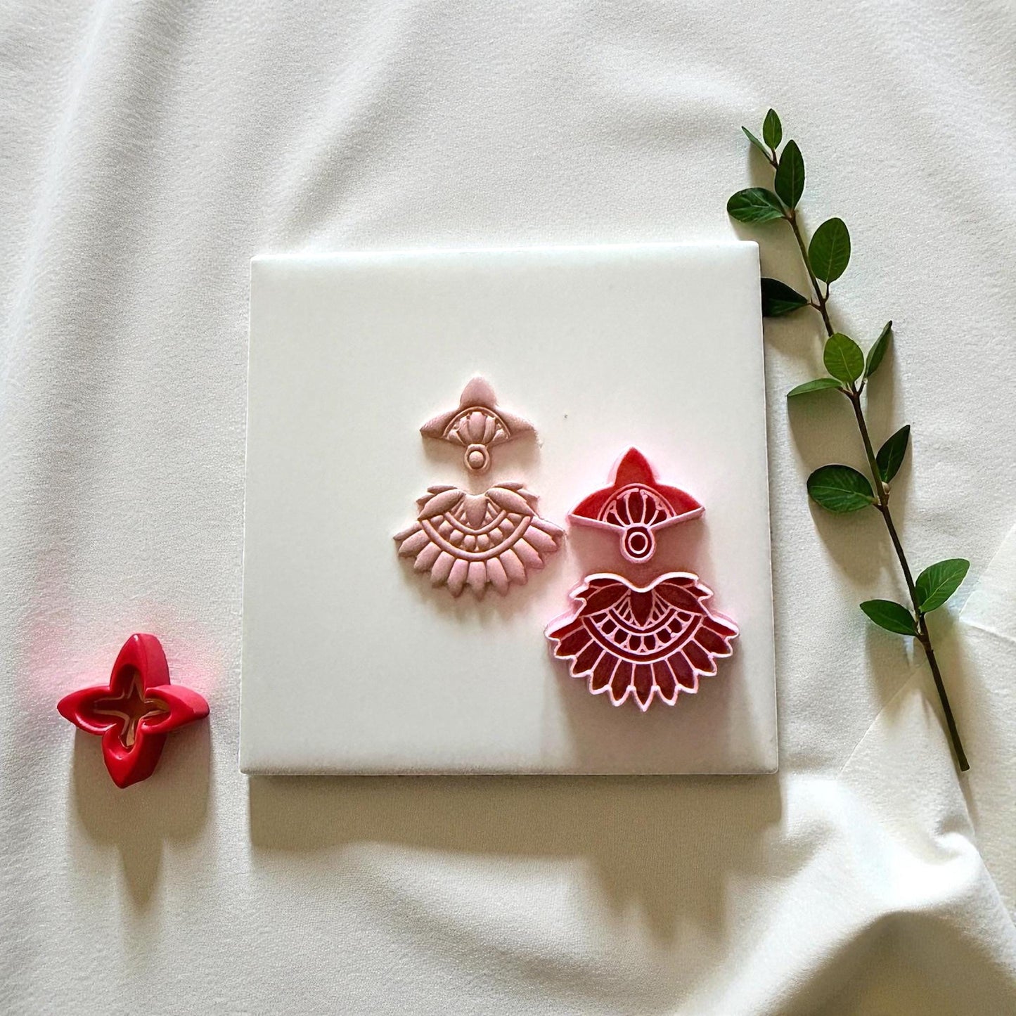Pink clay boho fan imprints beside red cutter on white tile with soft drape