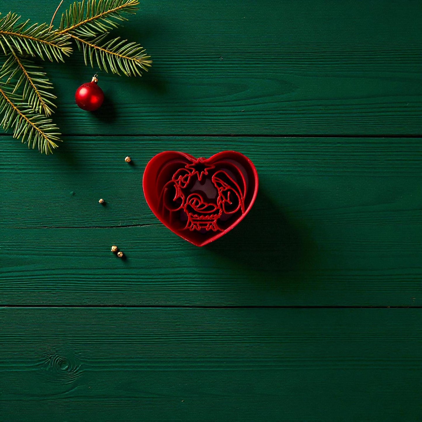 Red heart-shaped nativity polymer clay cutter on green wood with pine branch and ornament
