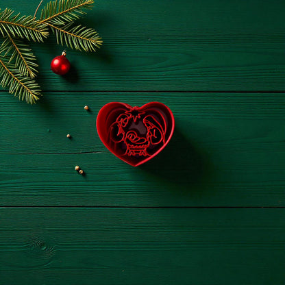 Red heart-shaped nativity polymer clay cutter on green wood with pine branch and ornament