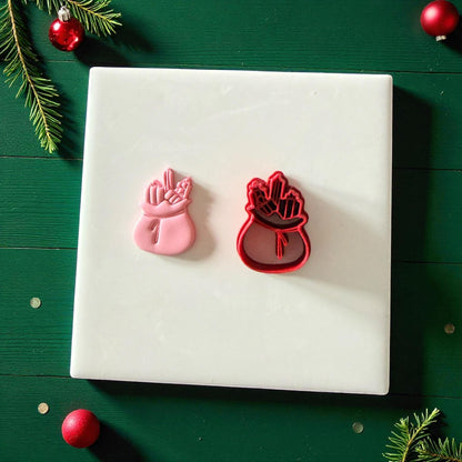 Santa’s sack cutter and clay imprint displayed on white tile surrounded by Christmas ornaments