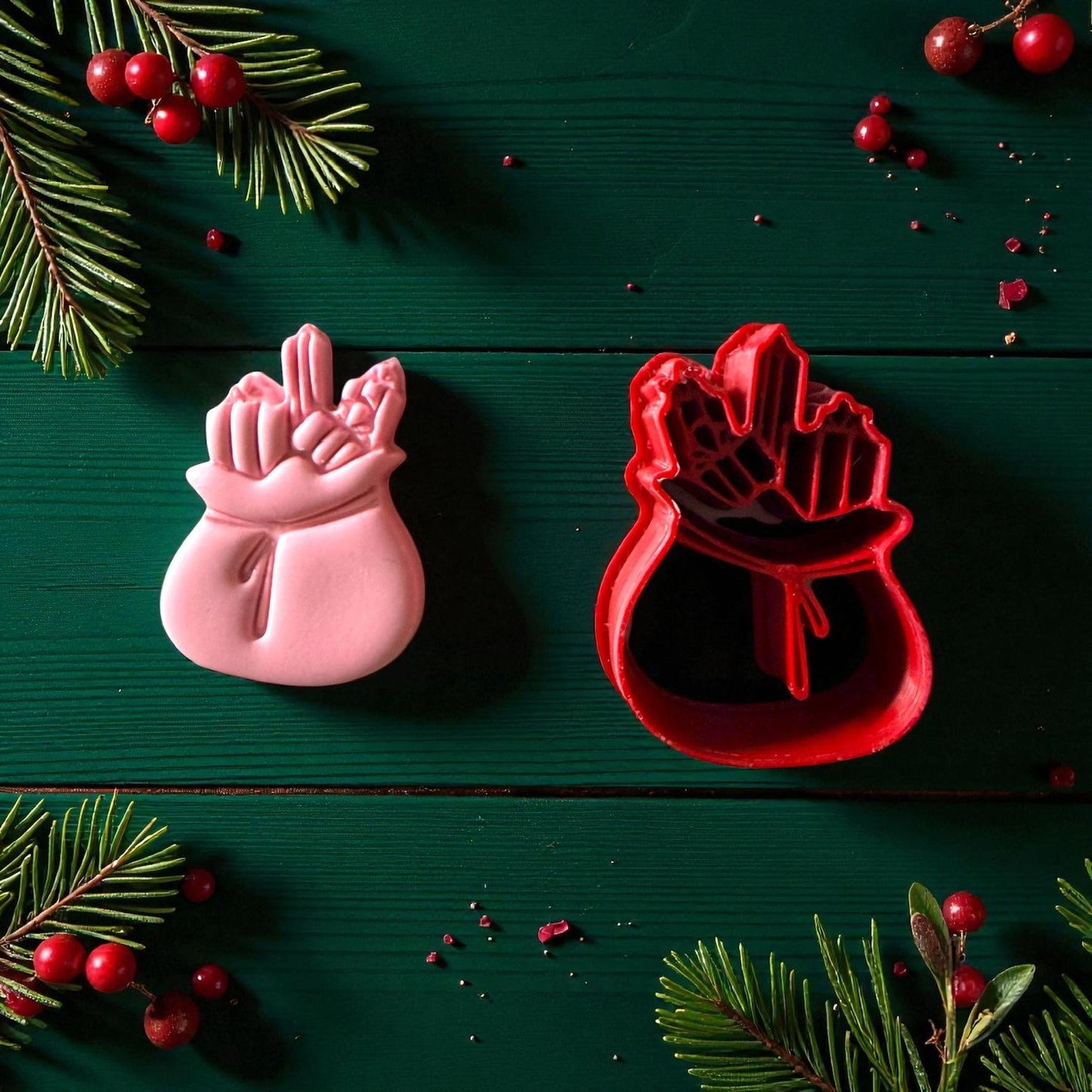 Pink Santa toy bag clay imprint beside red cutter with pine and berries