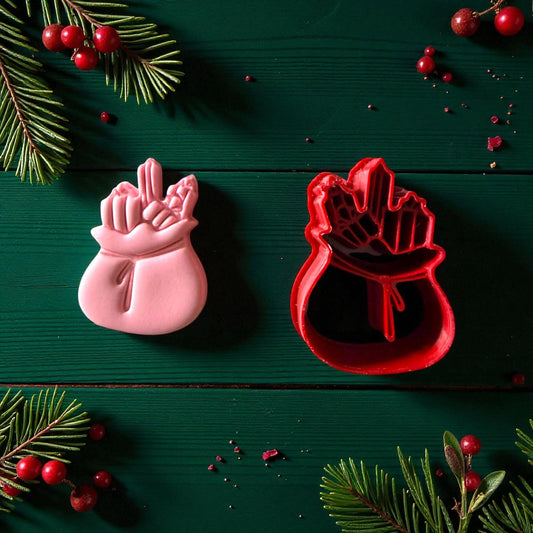 Pink Santa toy bag clay imprint beside red cutter with pine and berries
