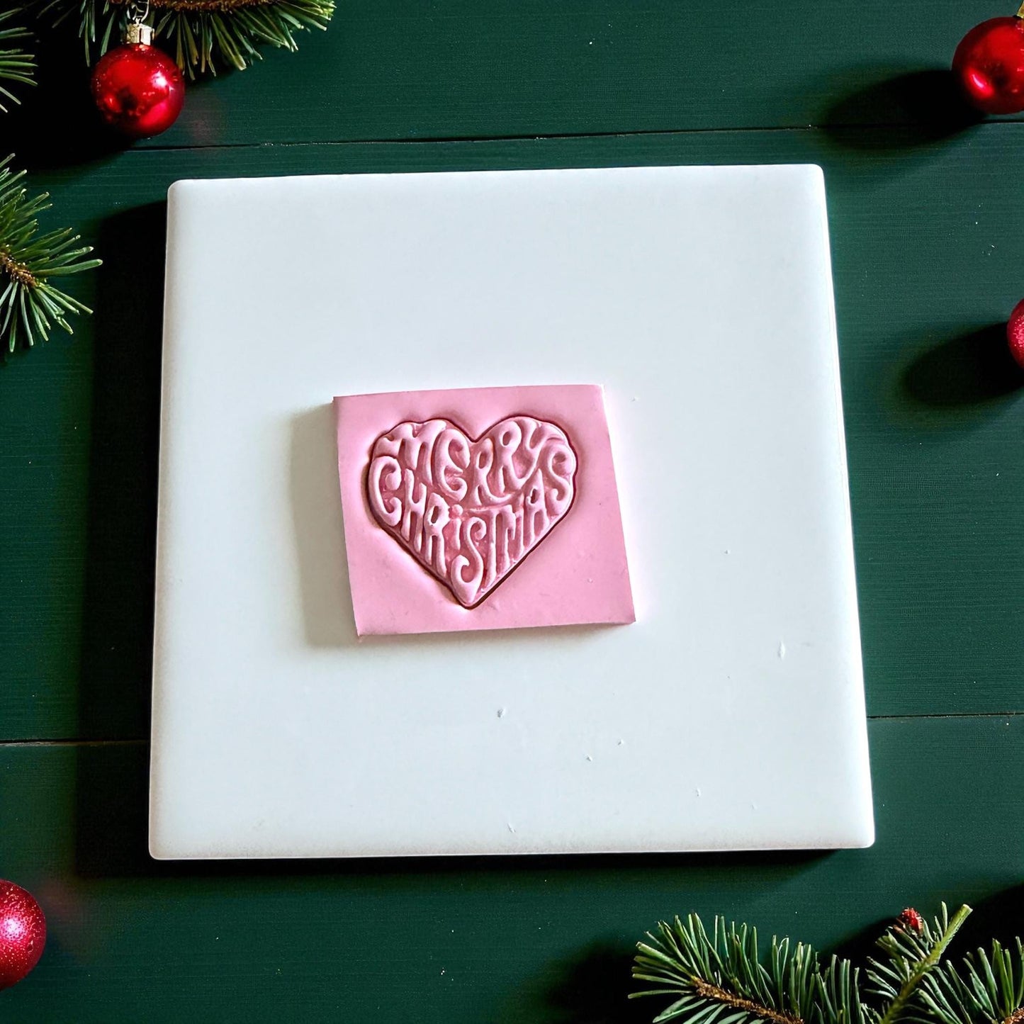 Pink clay square embossed with Merry Christmas heart design on white tile