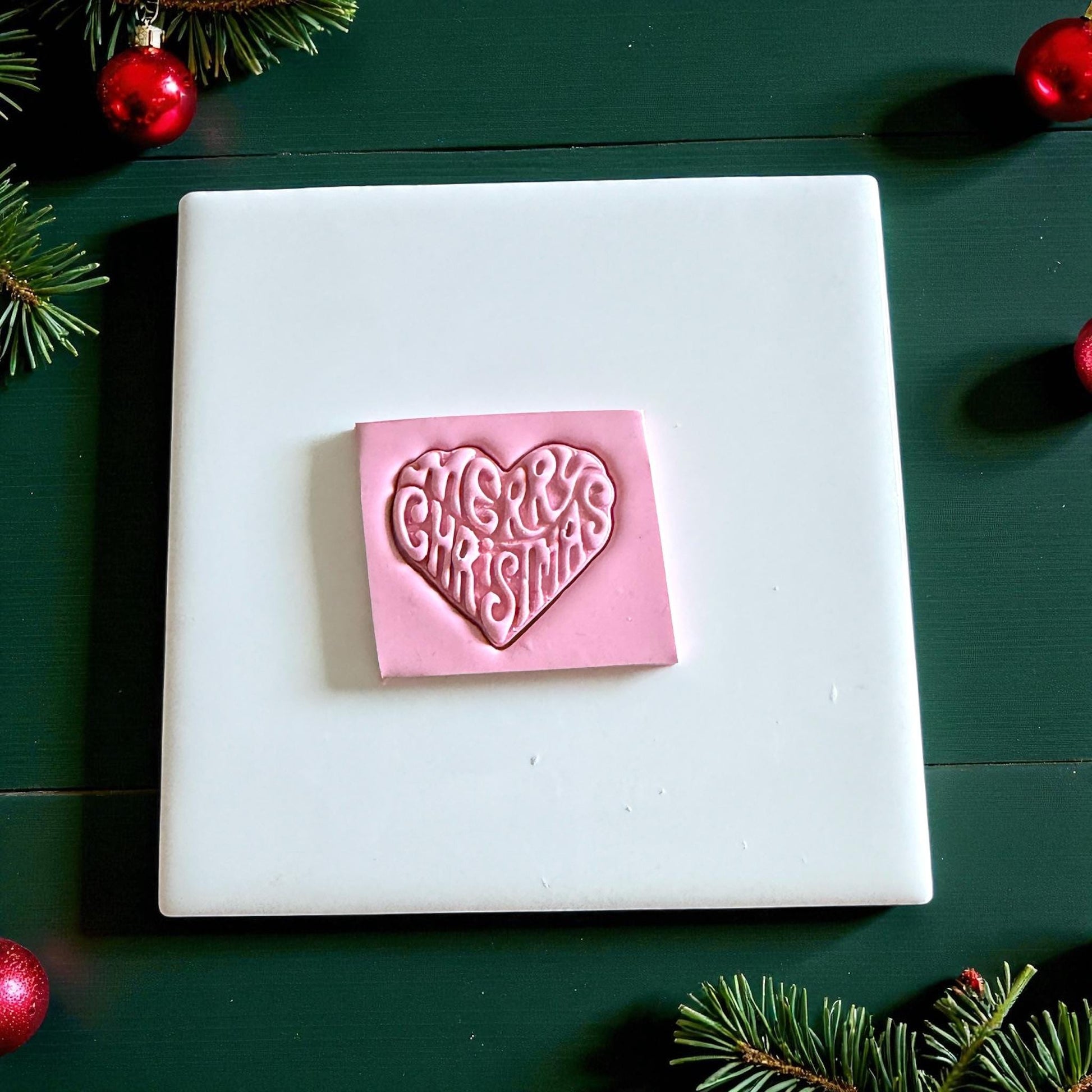 Pink clay square embossed with Merry Christmas heart design on white tile