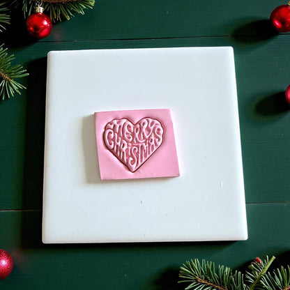 Pink clay square embossed with Merry Christmas heart design on white tile