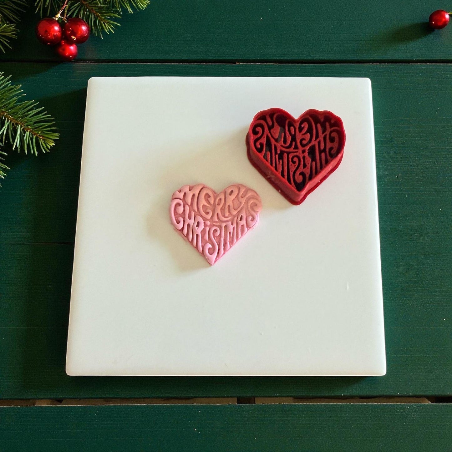 Red heart cutter beside pink clay heart imprint with Merry Christmas lettering