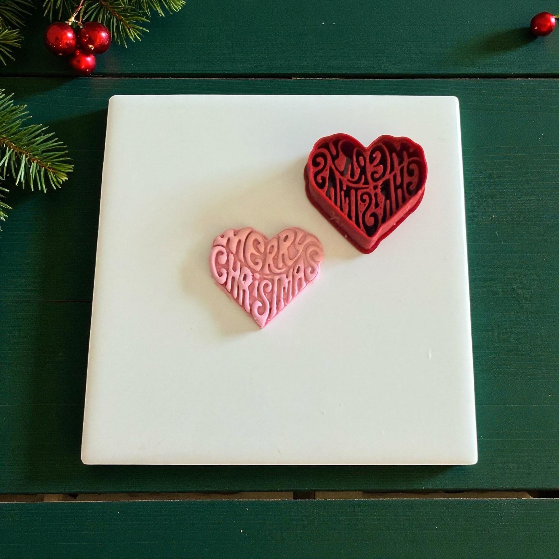 Red heart cutter beside pink clay heart imprint with Merry Christmas lettering