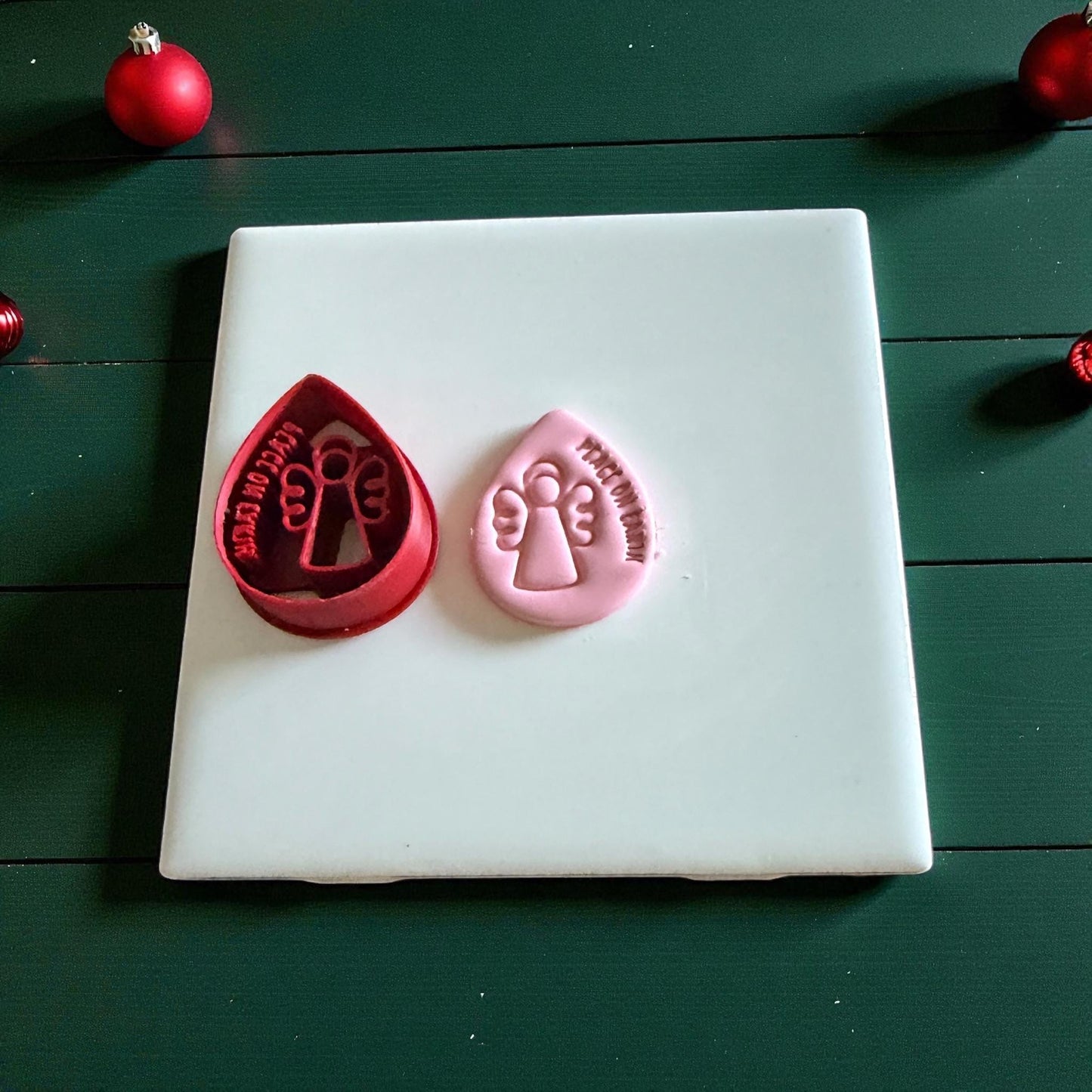 Red polymer clay cutter with angel shape on white tile background