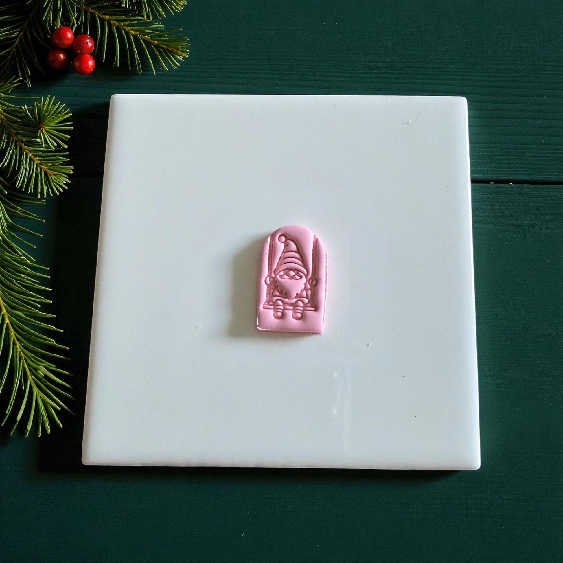 Small pink gnome on swing clay piece centered on white tile
