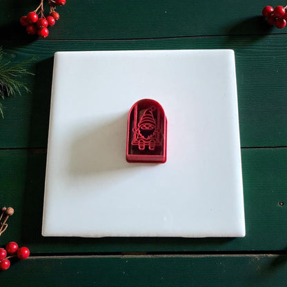 Red gnome cutter on white tile surrounded by red berries and pine sprigs
