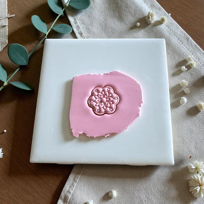 Pink clay with floral medallion impression on white tile with greenery