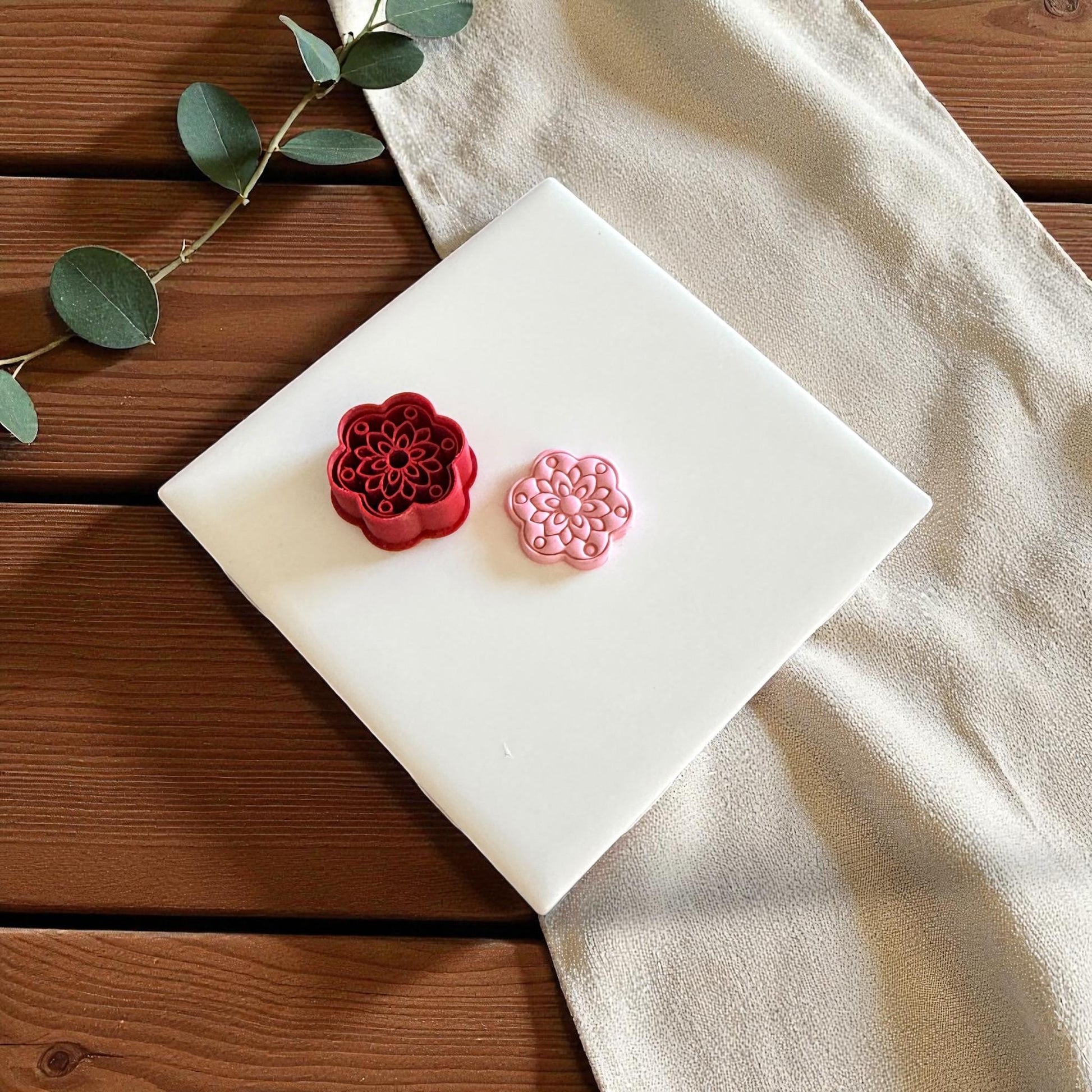 Red flower cutter and pink clay piece side by side on white tile