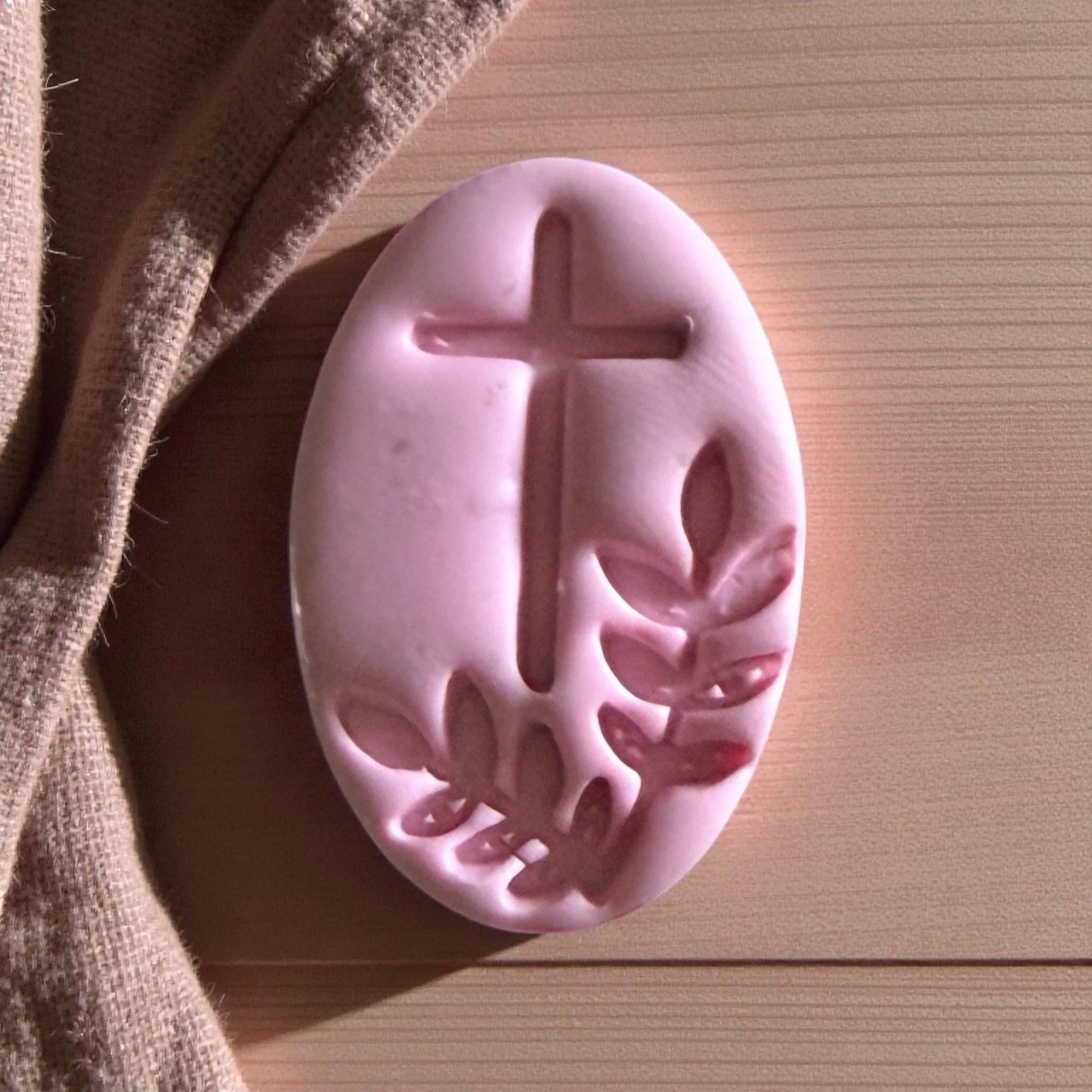 Close-up of pink oval clay featuring cross and olive branch pattern