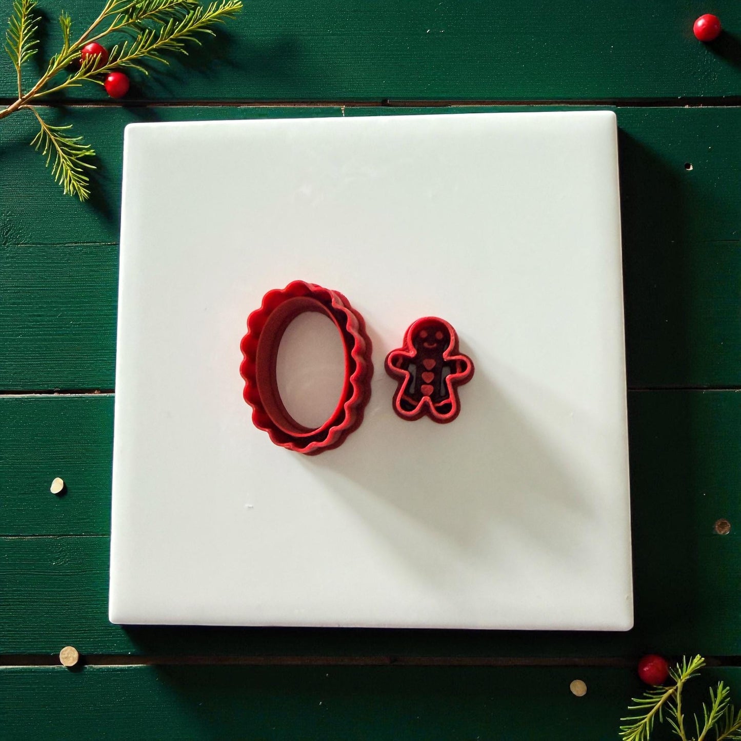 Red gingerbread and oval cutters on white tile with festive greenery