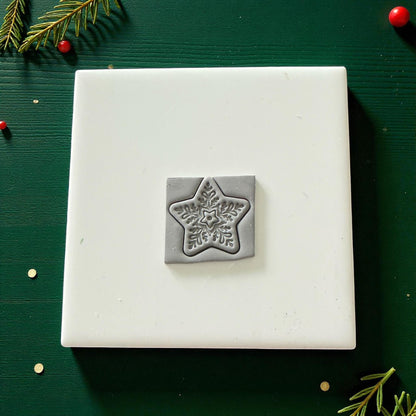 Square clay piece with star snowflake impression centered on white tile with holiday greenery