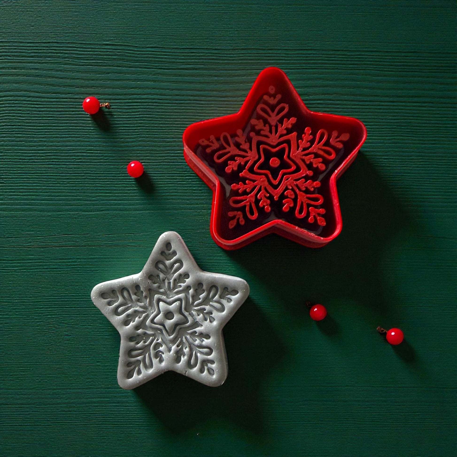 Red star cutter and gray clay snowflake star design side by side on green wood