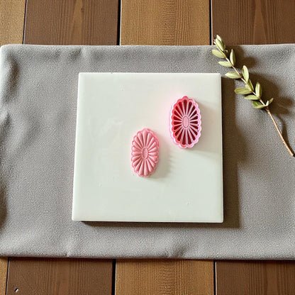 Two pink floral oval clay cutters and imprints on white tile with natural greenery
