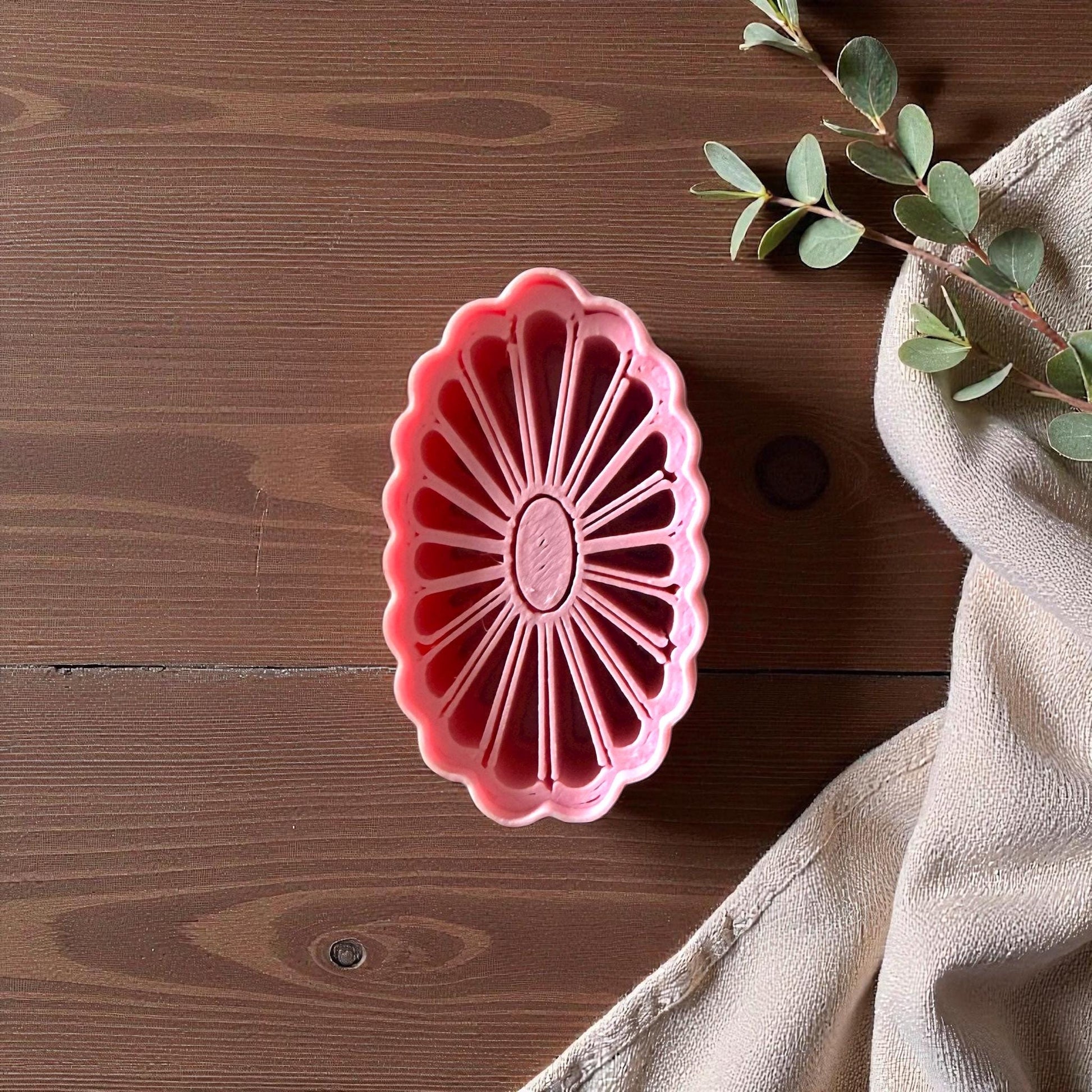 Oval daisy frame clay cutter centered on white tile with succulents and neutral background