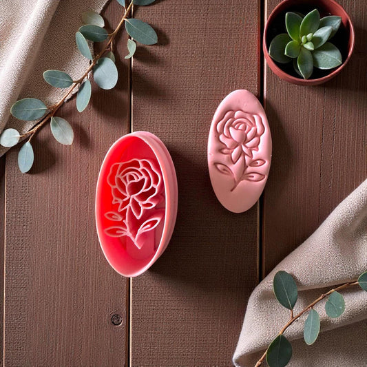 Rose cameo clay cutter beside matching pink clay imprint on wood with succulents and beige fabric