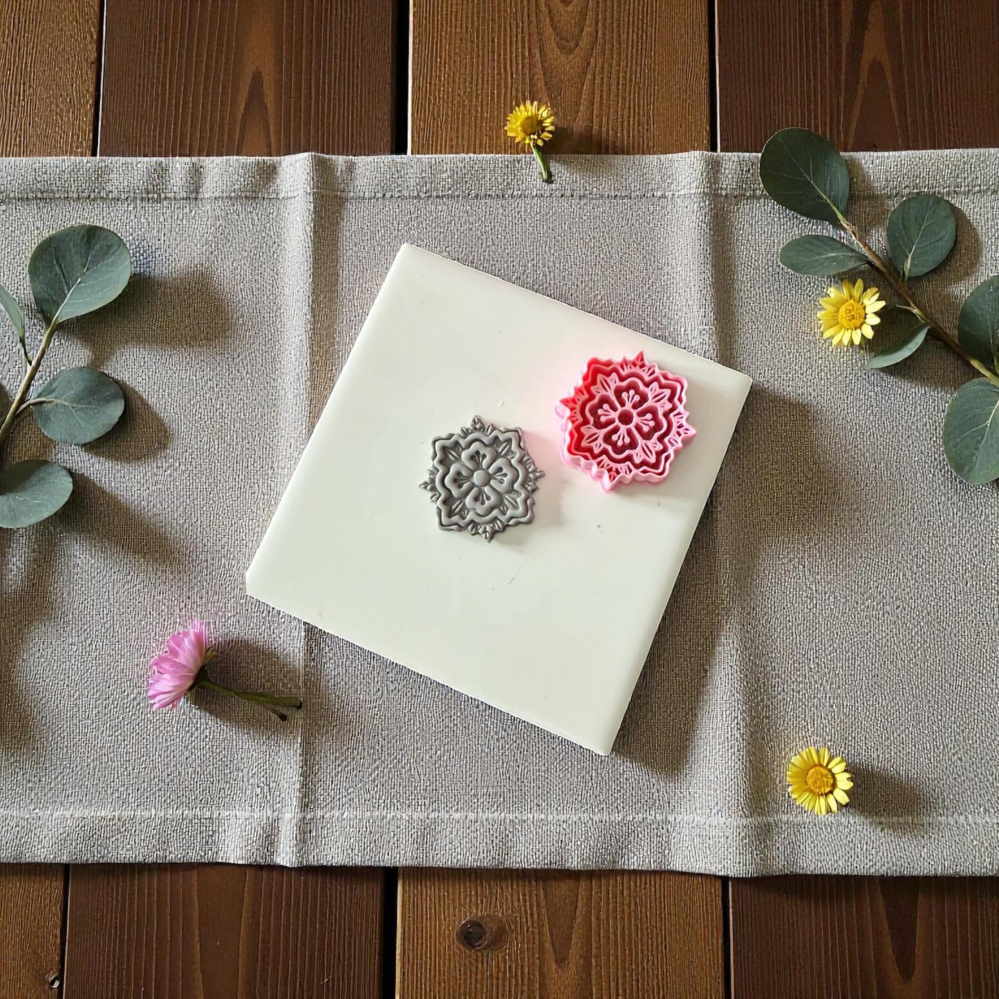 Pink and gray boho floral clay cutter and imprint on white tile with yellow flowers