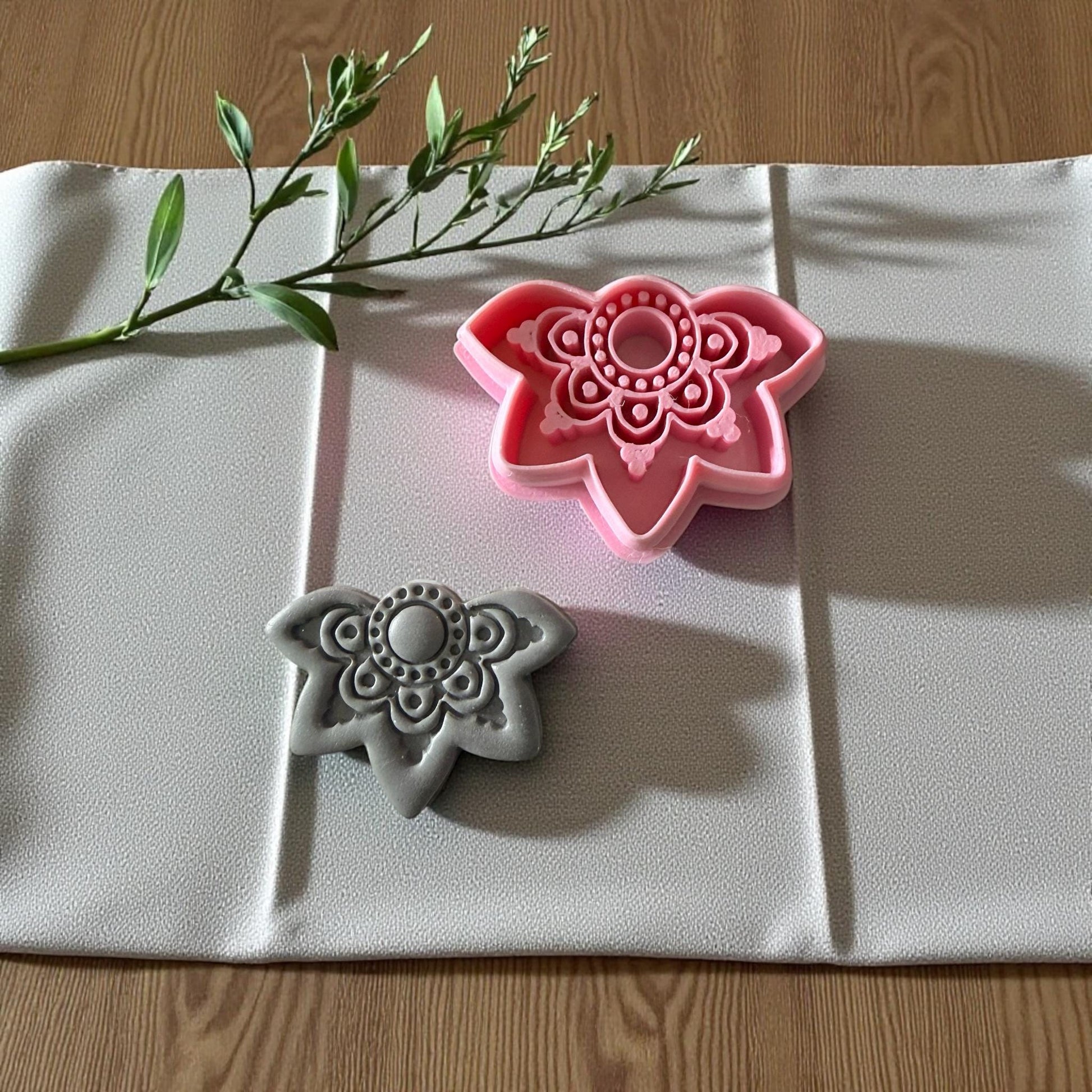 Boho floral cutter beside gray clay imprint on textured fabric