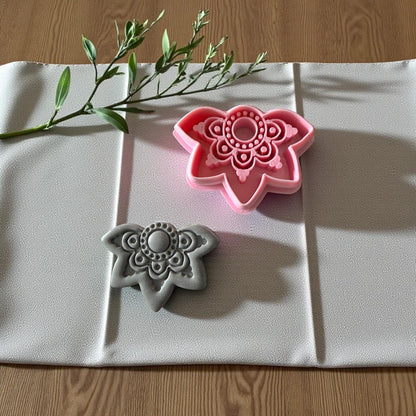 Boho floral cutter beside gray clay imprint on textured fabric